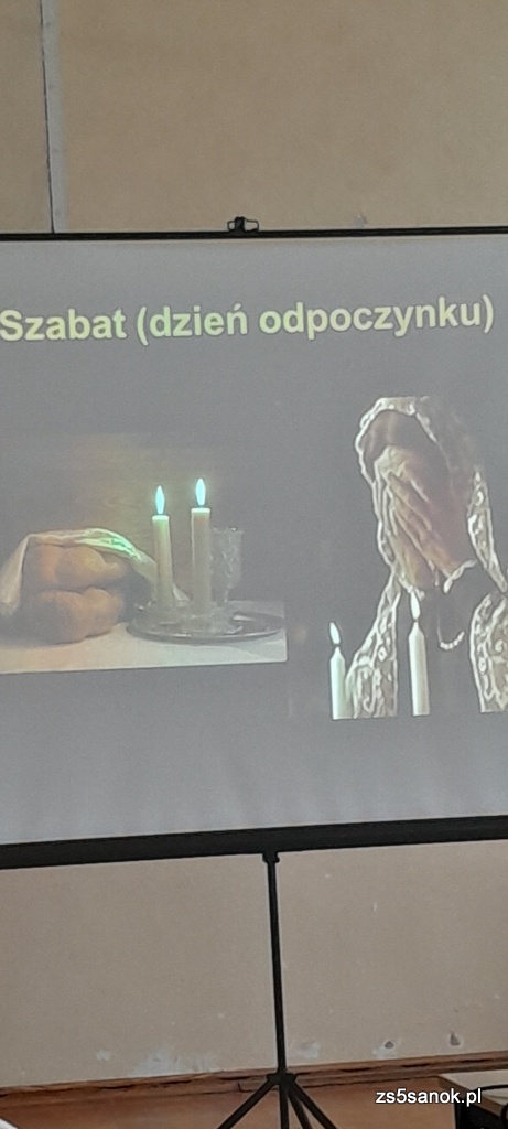  Obraz z projektora na którym jest kobieta z zasłoniętą twarzą, napis szabas dzień odpoczynku. 